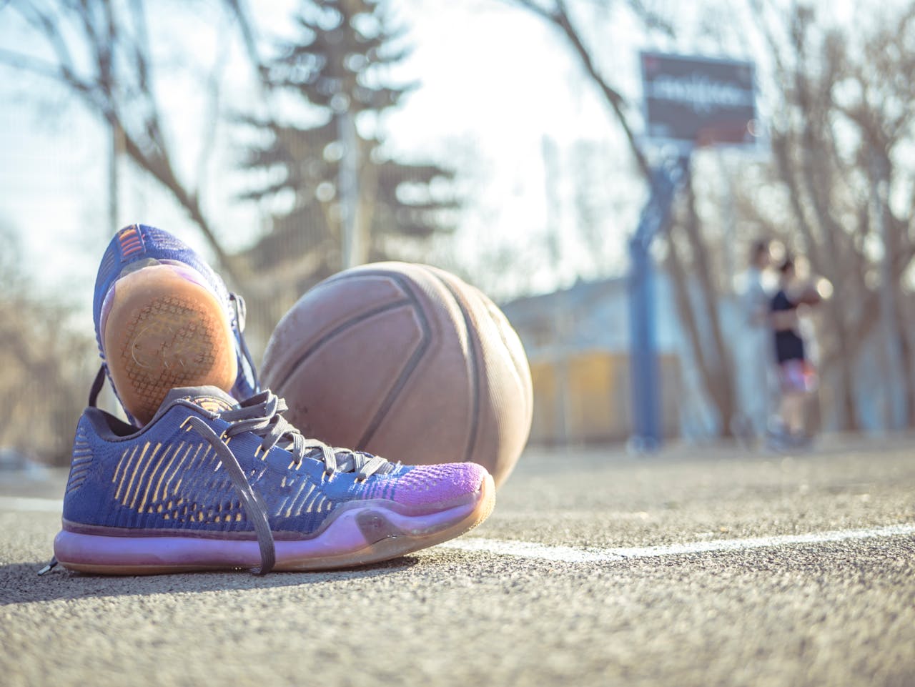 Detailed shot of sneakers next to a basketball on an outdoor court.